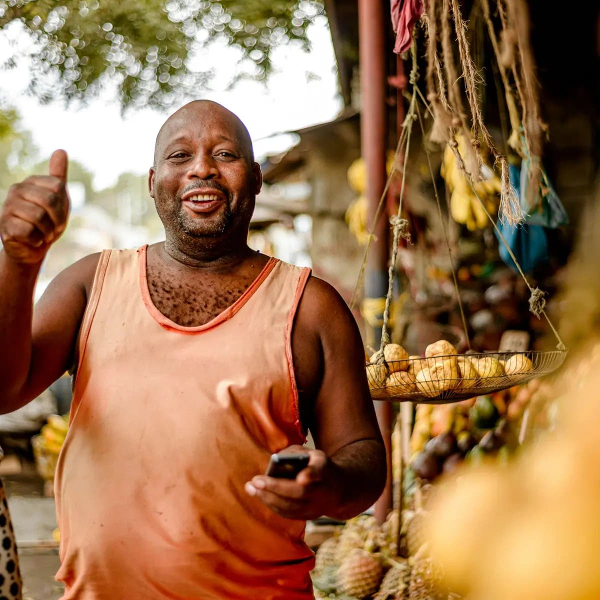 Muuza matunda sokoni akionyesha dole gumba huku ameshika simu