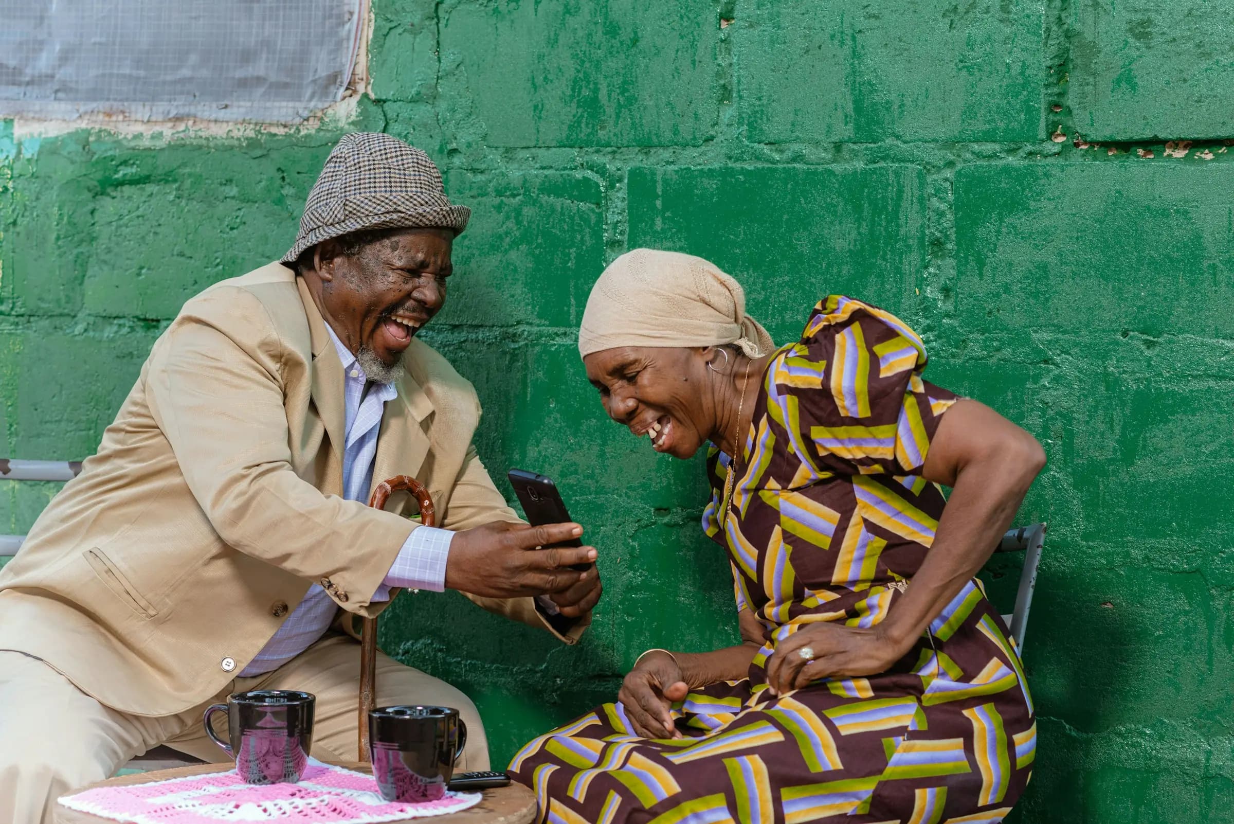 Wazee wawili wakicheka pamoja huku wakiangalia simu